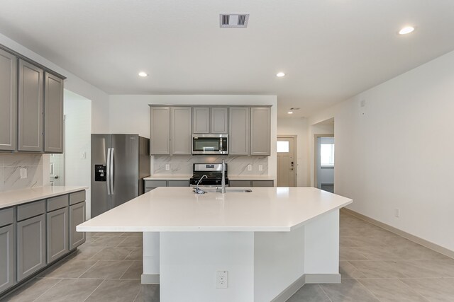 kitchen with stainless steel appliances, a center island with sink, and gray cabinetry