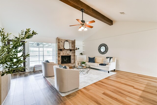 living room with ceiling fan, light wood-type flooring, brick wall, a brick fireplace, and beam ceiling