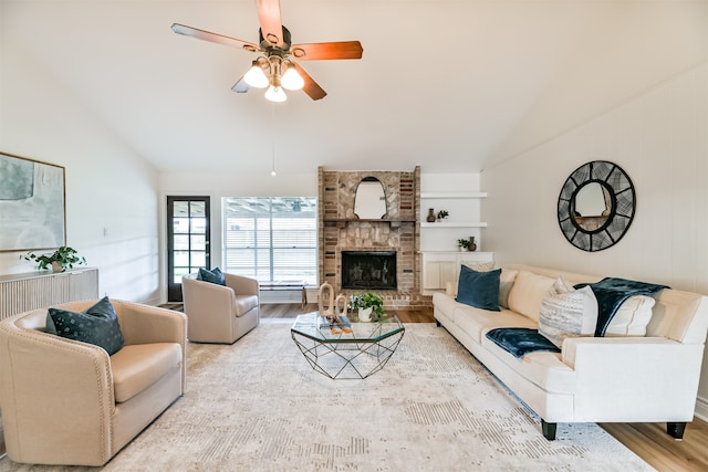 living room featuring light hardwood / wood-style flooring, vaulted ceiling, brick wall, ceiling fan, and a stone fireplace