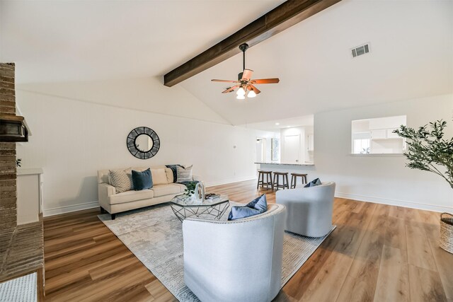 living room featuring light hardwood / wood-style floors, beam ceiling, ceiling fan, and a brick fireplace