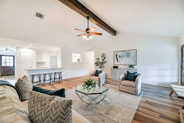 living room featuring ceiling fan, light hardwood / wood-style flooring, and vaulted ceiling with beams