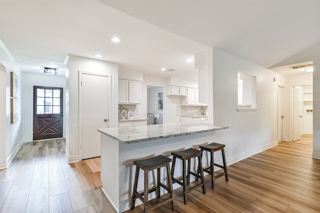 kitchen with light hardwood / wood-style flooring, backsplash, white cabinets, a breakfast bar, and kitchen peninsula