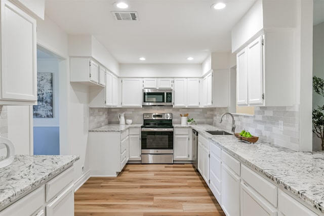 kitchen with appliances with stainless steel finishes, decorative backsplash, white cabinets, and light wood-type flooring