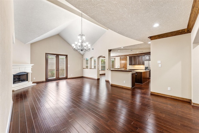 unfurnished living room with a fireplace with raised hearth, a chandelier, a textured ceiling, baseboards, and dark wood finished floors