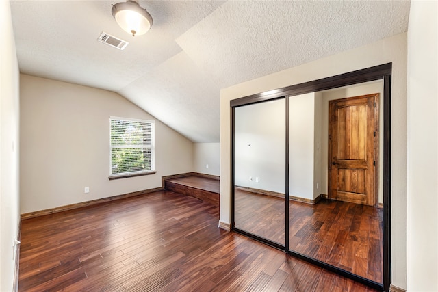 additional living space with visible vents, vaulted ceiling, a textured ceiling, and hardwood / wood-style flooring