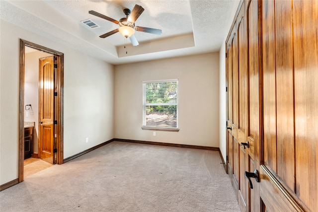 unfurnished bedroom featuring a raised ceiling, visible vents, light carpet, and a textured ceiling