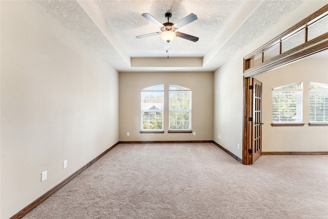 carpeted spare room with a ceiling fan, a tray ceiling, a textured ceiling, and baseboards