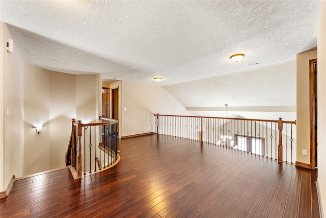 interior space with a textured ceiling, wood finished floors, visible vents, baseboards, and vaulted ceiling