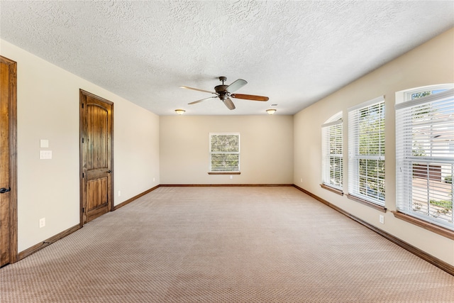 empty room featuring a ceiling fan, light colored carpet, a textured ceiling, and baseboards