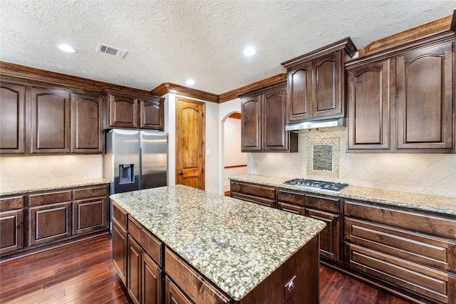 kitchen featuring under cabinet range hood, stainless steel appliances, dark wood-type flooring, visible vents, and a center island