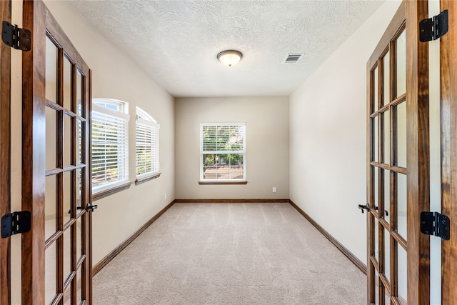 unfurnished room featuring baseboards, french doors, visible vents, and light colored carpet