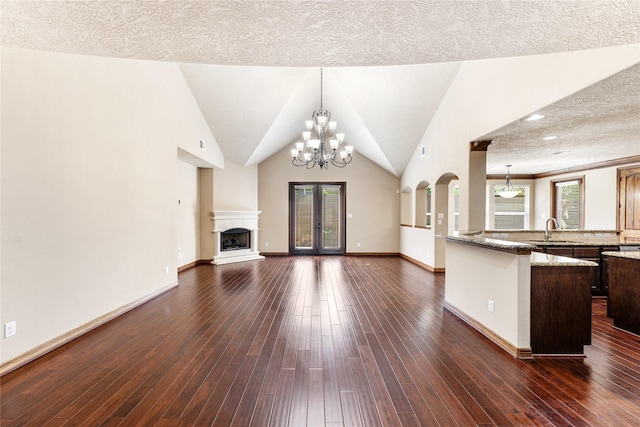 unfurnished living room with a fireplace with raised hearth, dark wood-type flooring, a sink, a chandelier, and baseboards