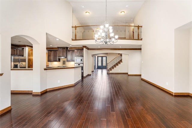 unfurnished living room with arched walkways, dark wood-style flooring, baseboards, and an inviting chandelier