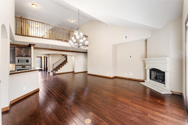 unfurnished living room with a notable chandelier, a fireplace with raised hearth, visible vents, dark wood-type flooring, and stairs