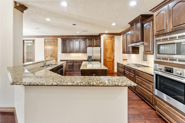 kitchen with dark wood-style floors, light stone counters, a kitchen island with sink, stainless steel appliances, and a sink