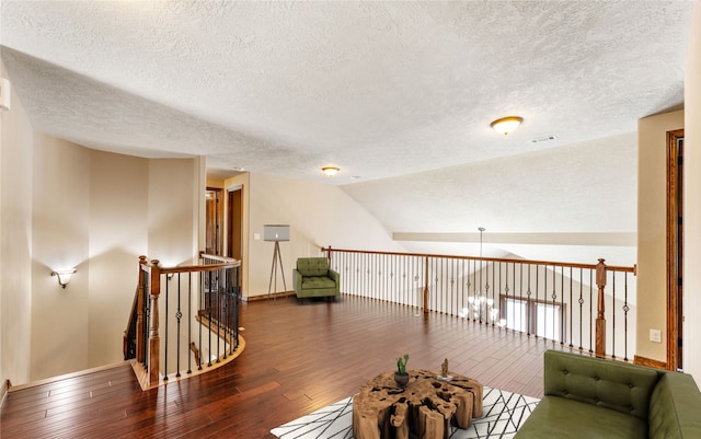 sitting room with lofted ceiling, hardwood / wood-style flooring, a textured ceiling, and an upstairs landing