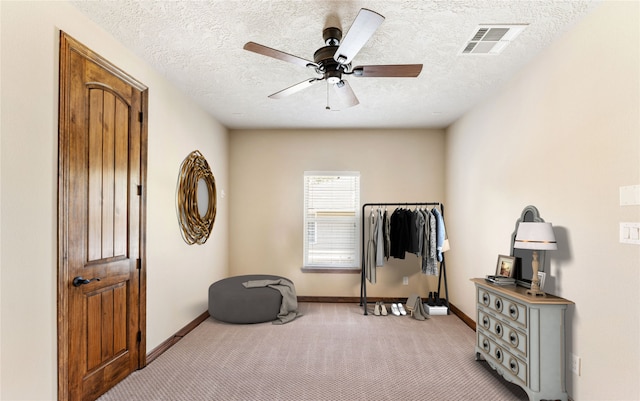 interior space featuring a textured ceiling, visible vents, baseboards, a ceiling fan, and carpet