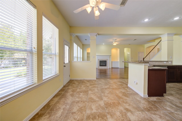 kitchen featuring ceiling fan, light stone counters, dark brown cabinetry, and ornate columns