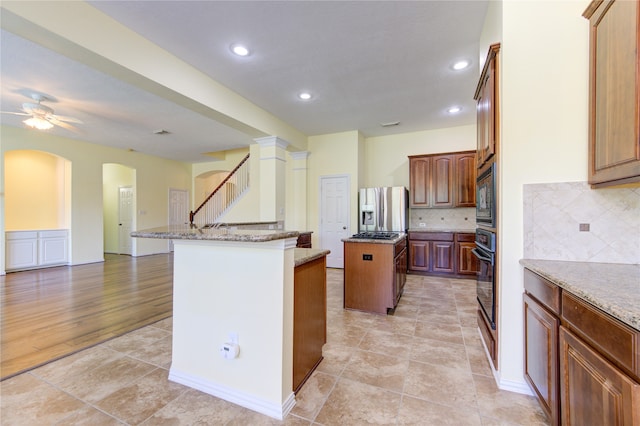 kitchen featuring light hardwood / wood-style flooring, black appliances, a center island, ceiling fan, and light stone counters