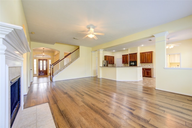 unfurnished living room featuring light hardwood / wood-style flooring, ceiling fan with notable chandelier, decorative columns, and a fireplace