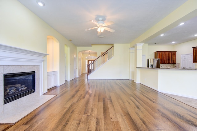 unfurnished living room with ceiling fan, a tiled fireplace, and light hardwood / wood-style floors