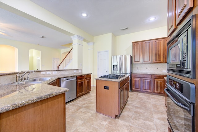 kitchen featuring black appliances, a center island, light stone countertops, sink, and ornate columns