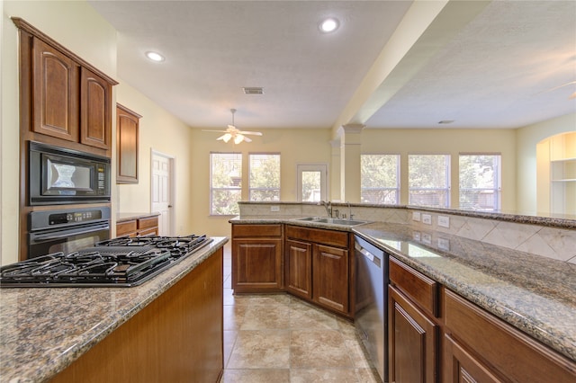 kitchen with ornate columns, stainless steel appliances, sink, ceiling fan, and stone counters