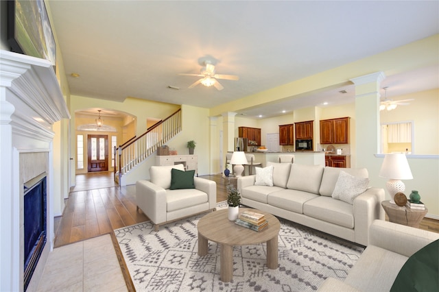 living area featuring arched walkways, a ceiling fan, stairs, ornate columns, and light tile patterned flooring