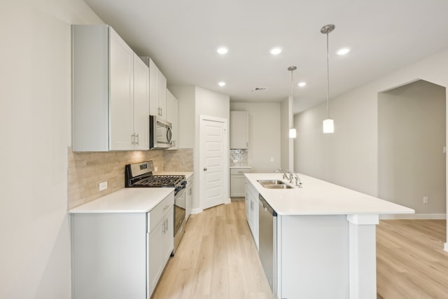 kitchen featuring a center island with sink, appliances with stainless steel finishes, pendant lighting, sink, and light hardwood / wood-style floors