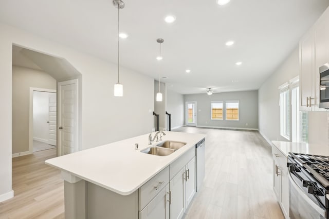 kitchen with light hardwood / wood-style flooring, sink, an island with sink, pendant lighting, and appliances with stainless steel finishes