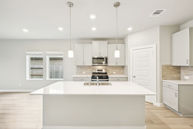 kitchen featuring stainless steel appliances, hanging light fixtures, sink, and light hardwood / wood-style flooring