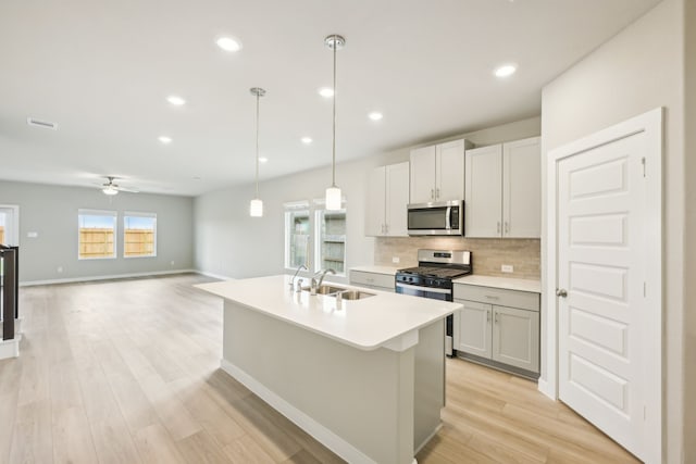 kitchen with light hardwood / wood-style flooring, appliances with stainless steel finishes, hanging light fixtures, and a kitchen island with sink