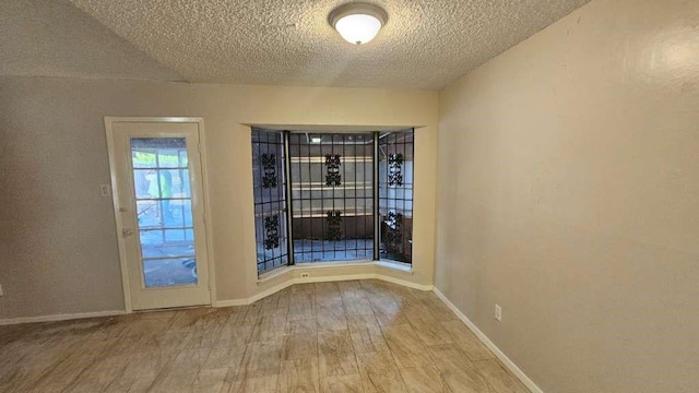 unfurnished room with wood finished floors, a textured ceiling, and baseboards