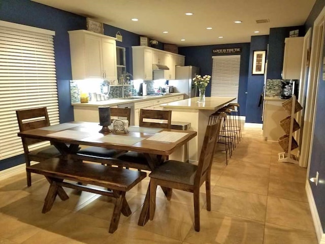 kitchen featuring ventilation hood, a breakfast bar, light tile patterned floors, white cabinets, and stainless steel refrigerator