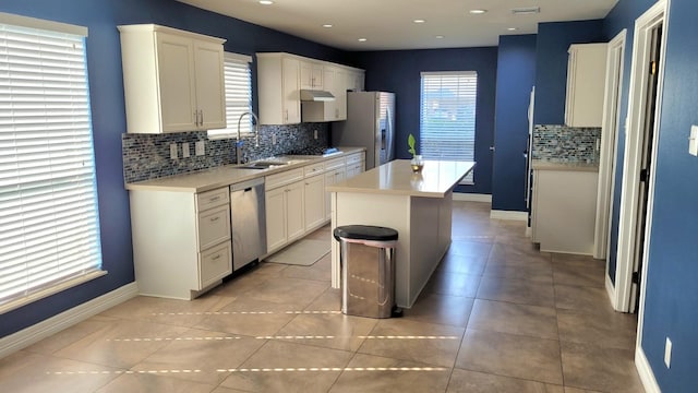 kitchen featuring a kitchen island, stainless steel appliances, backsplash, sink, and white cabinetry