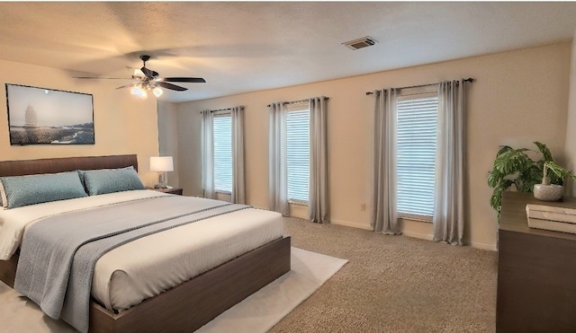 carpeted bedroom with a textured ceiling, multiple windows, and ceiling fan