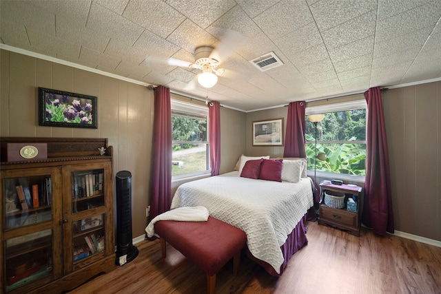 bedroom featuring ceiling fan, multiple windows, ornamental molding, and hardwood / wood-style flooring