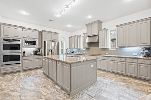 kitchen with appliances with stainless steel finishes, a kitchen island with sink, gray cabinetry, and backsplash