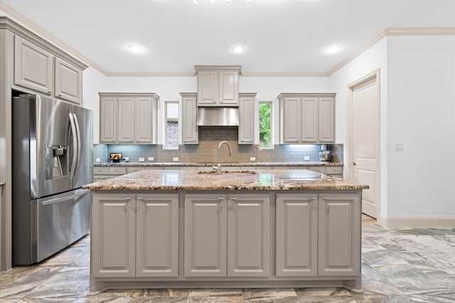 kitchen featuring gray cabinets, a kitchen island with sink, light stone countertops, light tile patterned floors, and stainless steel fridge