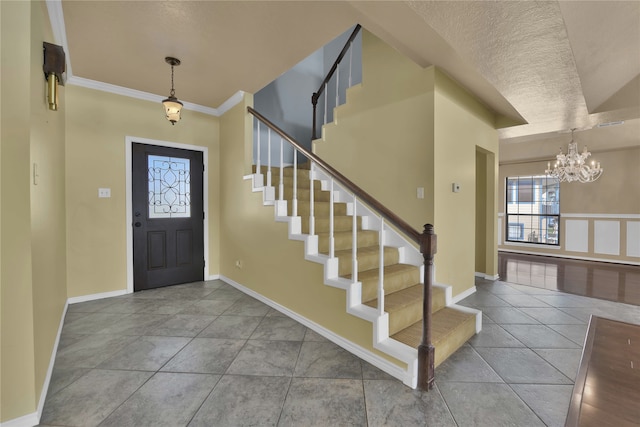 tiled foyer entrance with ornamental molding, a textured ceiling, and a chandelier