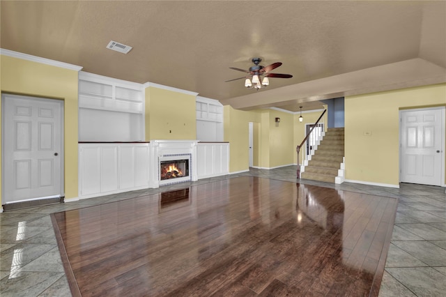 unfurnished living room featuring ceiling fan, built in shelves, a textured ceiling, and tile patterned flooring