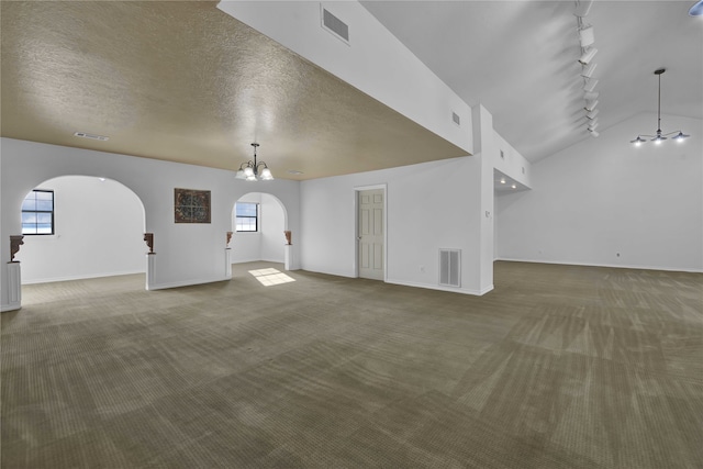 unfurnished living room featuring carpet, vaulted ceiling, rail lighting, a textured ceiling, and an inviting chandelier