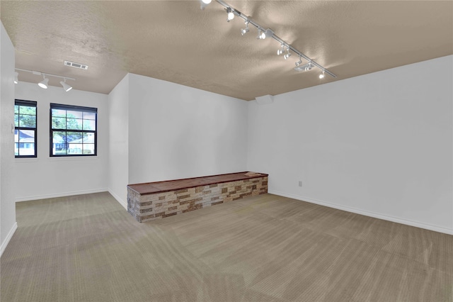 carpeted empty room featuring a textured ceiling and track lighting