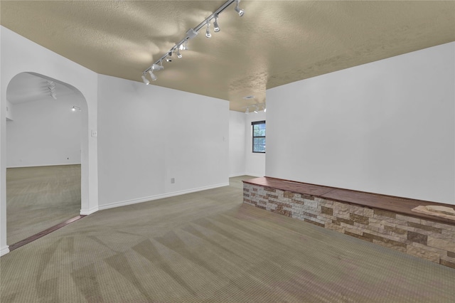 empty room with a textured ceiling, carpet flooring, and track lighting