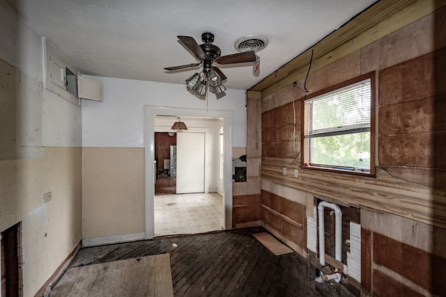 interior space featuring ceiling fan, wood-type flooring, wooden walls, and a textured ceiling