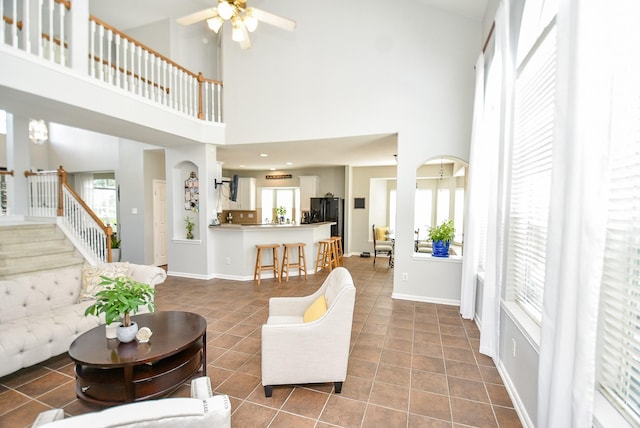 tiled living room with baseboards, stairs, arched walkways, and a ceiling fan