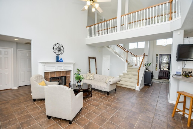 living area with a ceiling fan, a towering ceiling, stairs, baseboards, and a tiled fireplace