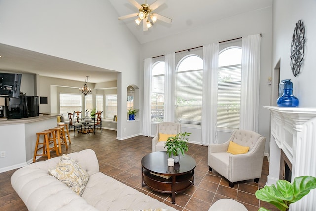 living room with high vaulted ceiling, ceiling fan with notable chandelier, dark tile patterned floors, a fireplace, and baseboards