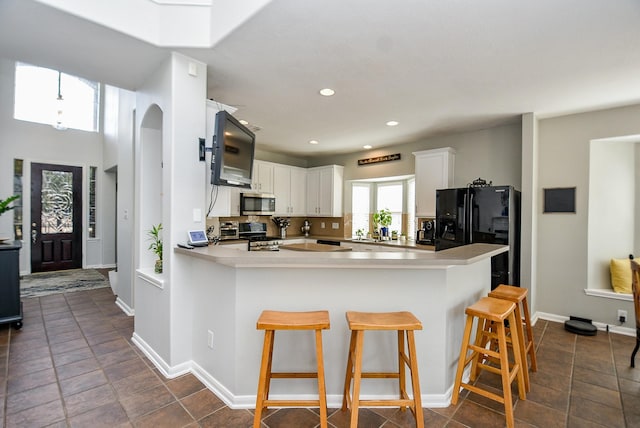 kitchen with arched walkways, a breakfast bar, stainless steel appliances, white cabinetry, and a peninsula