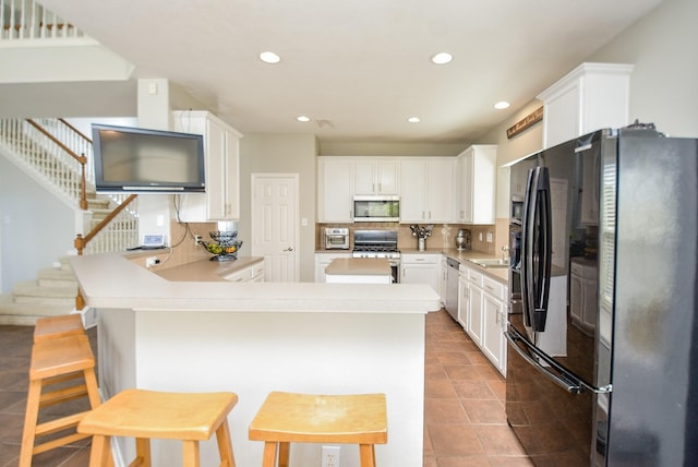 kitchen with stainless steel appliances, backsplash, white cabinets, and a peninsula